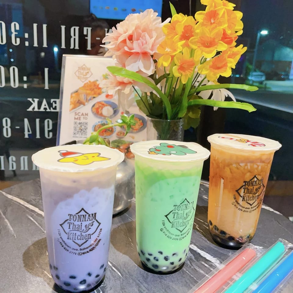 Three Tonnam Thai Kitchen bubble teas with character lids, flowers, and a menu on a table.
