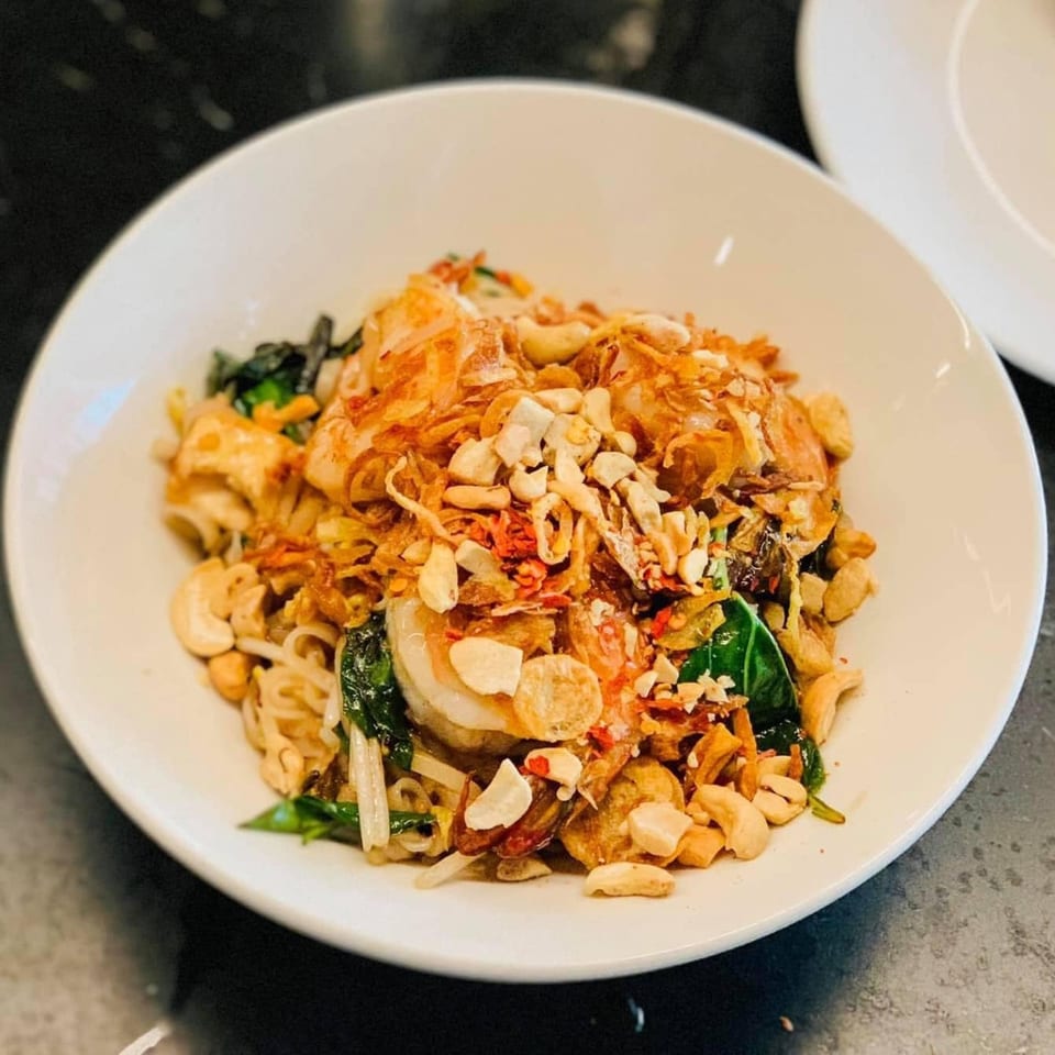 A white bowl filled with Pad Thai, topped with cashews, fried onions, and green herbs.