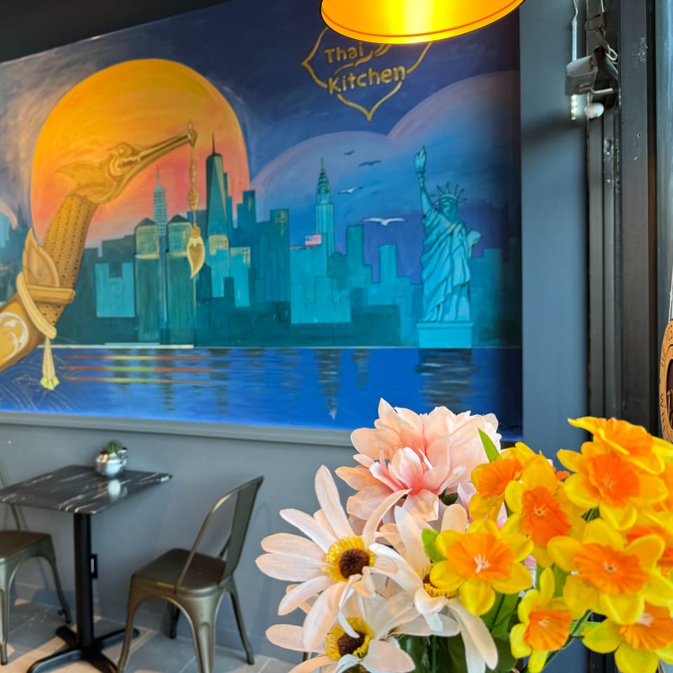 A mural of a city skyline with the Statue of Liberty and a Thai Kitchen logo, with flowers in the foreground.