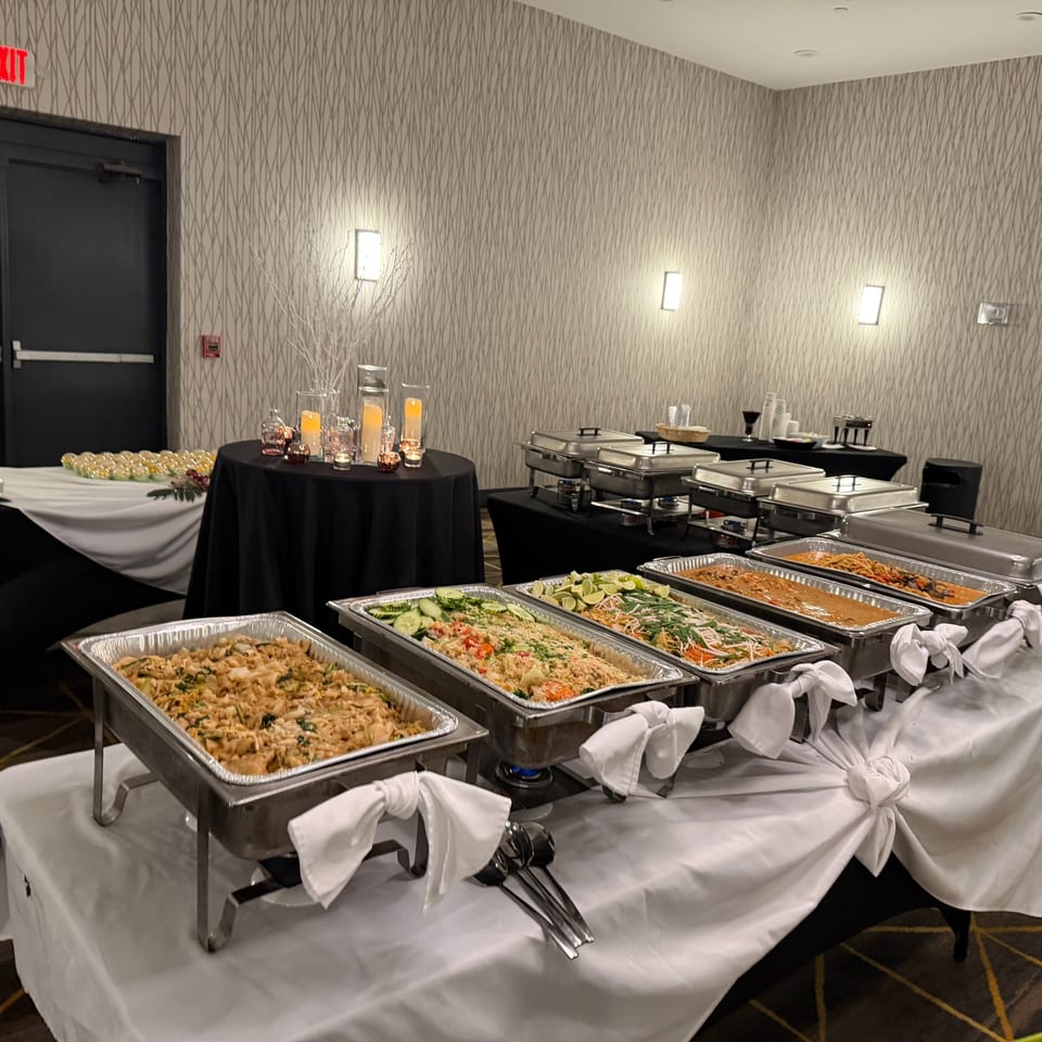 A buffet line with several chafing dishes filled with various Thai dishes, including noodles and rice.