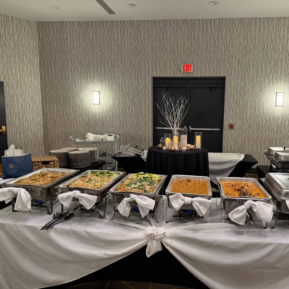 A buffet table with several chafing dishes filled with various Thai dishes, plates, and cutlery.