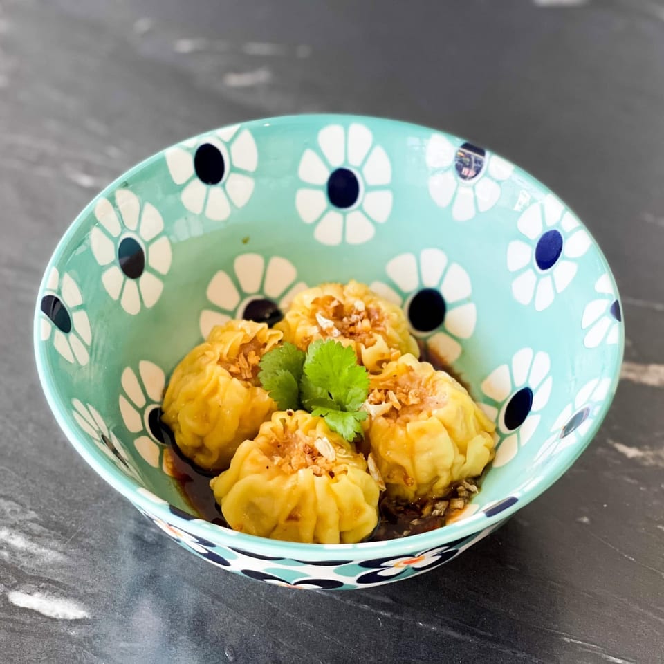 Four steamed dumplings with sauce, garlic, and cilantro in a floral teal bowl.