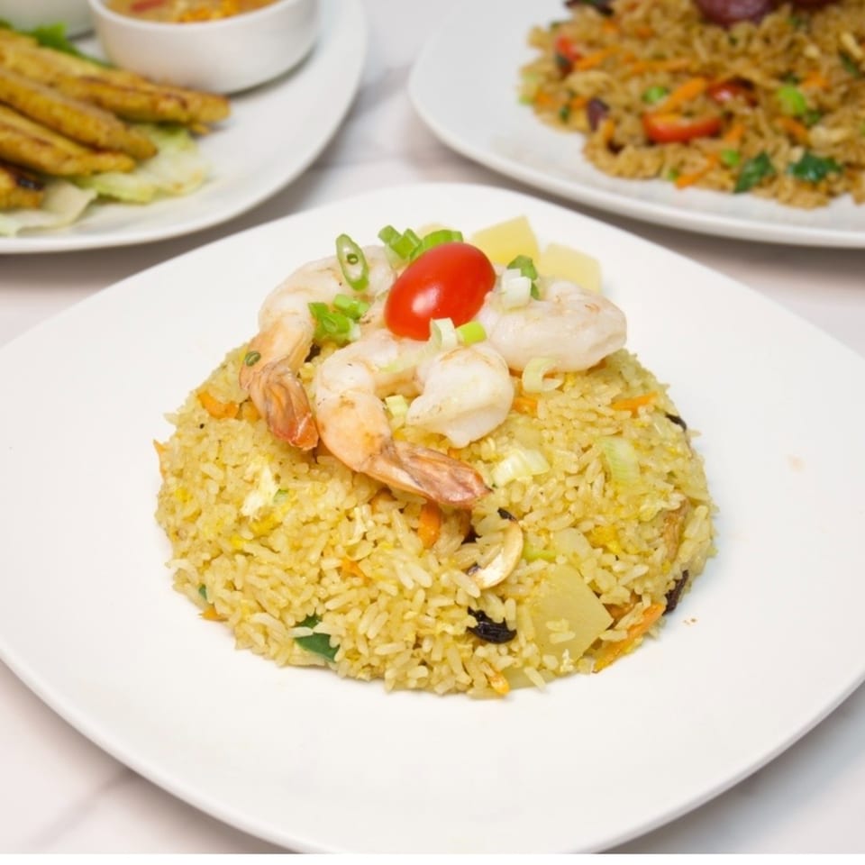 Pineapple fried rice with shrimp, cherry tomato, and green onions on a white plate.