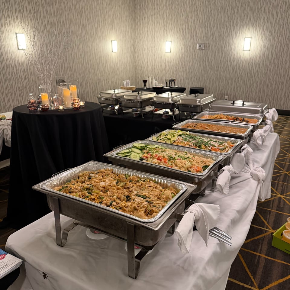 A buffet line with several chafing dishes filled with various Thai dishes, including noodles, rice, and curries.