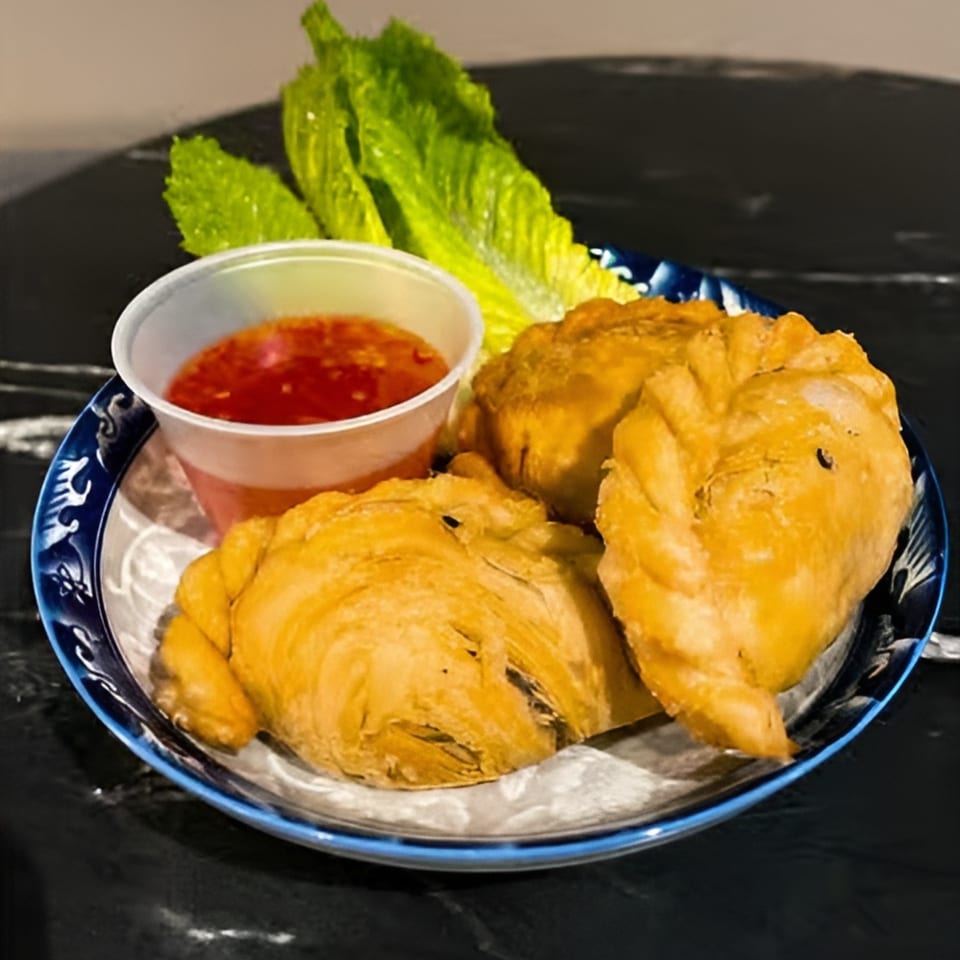 Three golden-brown curry puffs with a side of sweet chili sauce and lettuce on a blue-rimmed plate.