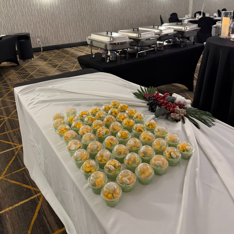 Dessert cups with green pudding, mango, and heart-shaped candies on a white-draped table.